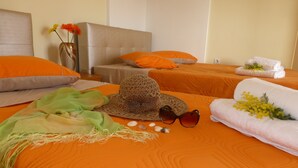 A hotel room with two beds, orange bedding, a woven hat, sunglasses, seashells, and towels with yellow flowers. - Pavloudis Apartments (Polygyros)