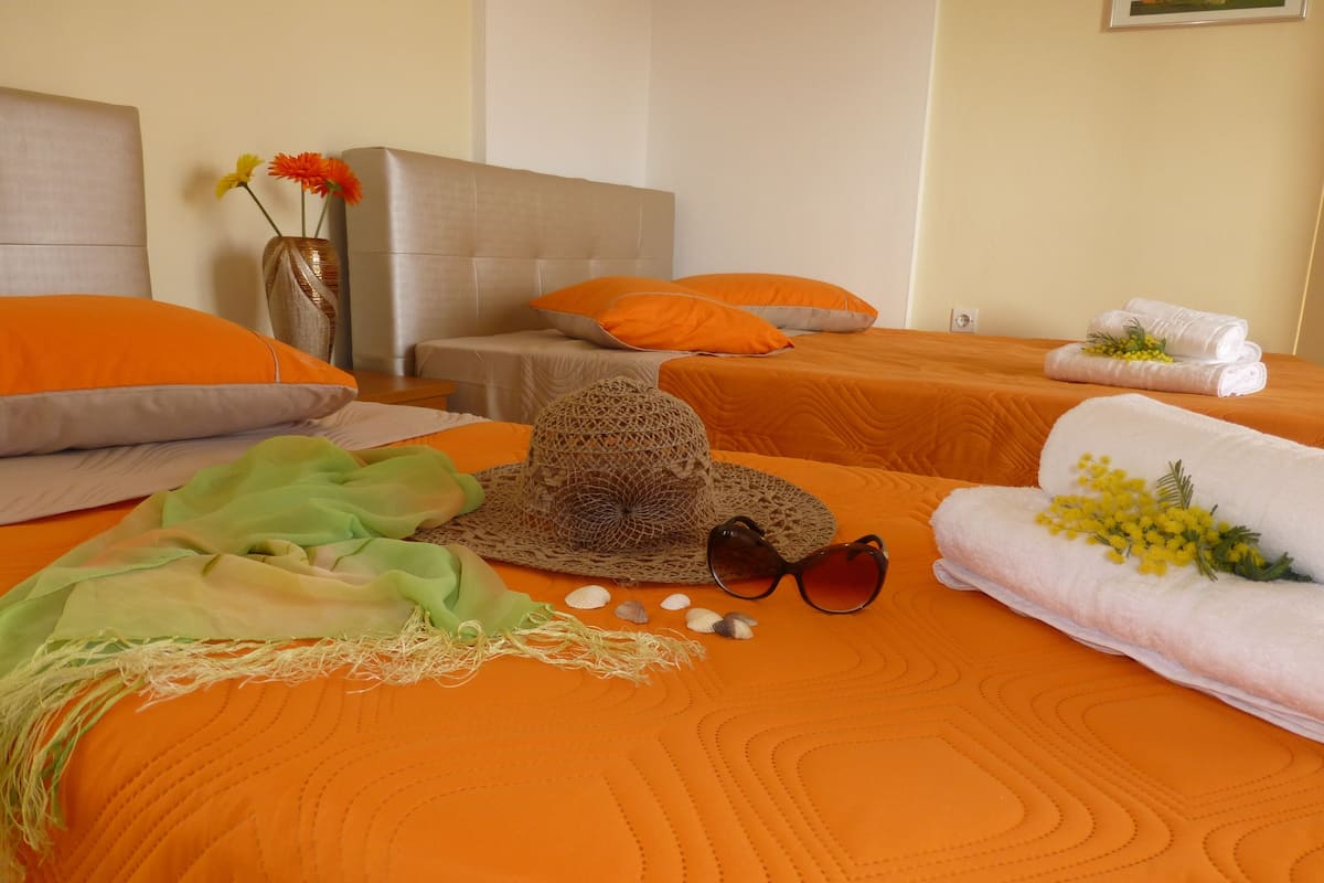 A hotel room with two beds, orange bedding, a woven hat, sunglasses, seashells, and towels with yellow flowers.
