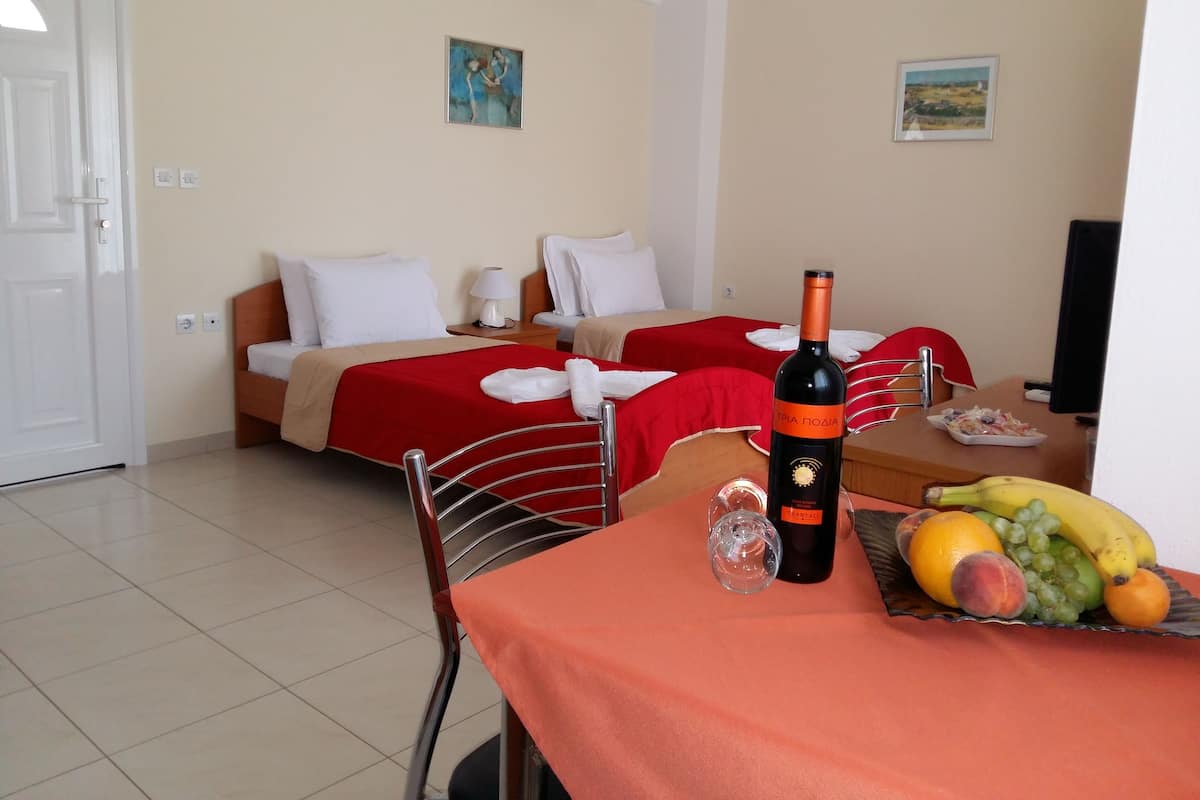 A hotel room with two beds, a dining table with a bottle of wine, and a fruit basket.