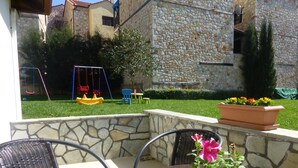 An outdoor patio with stone walls, a round table, wicker chairs, a swing set, and a flower planter. - Pavloudis Apartments (Polygyros)