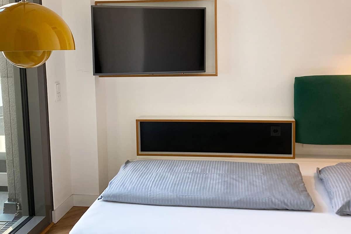 A modern hotel room with a bed, a mounted TV, and a window.