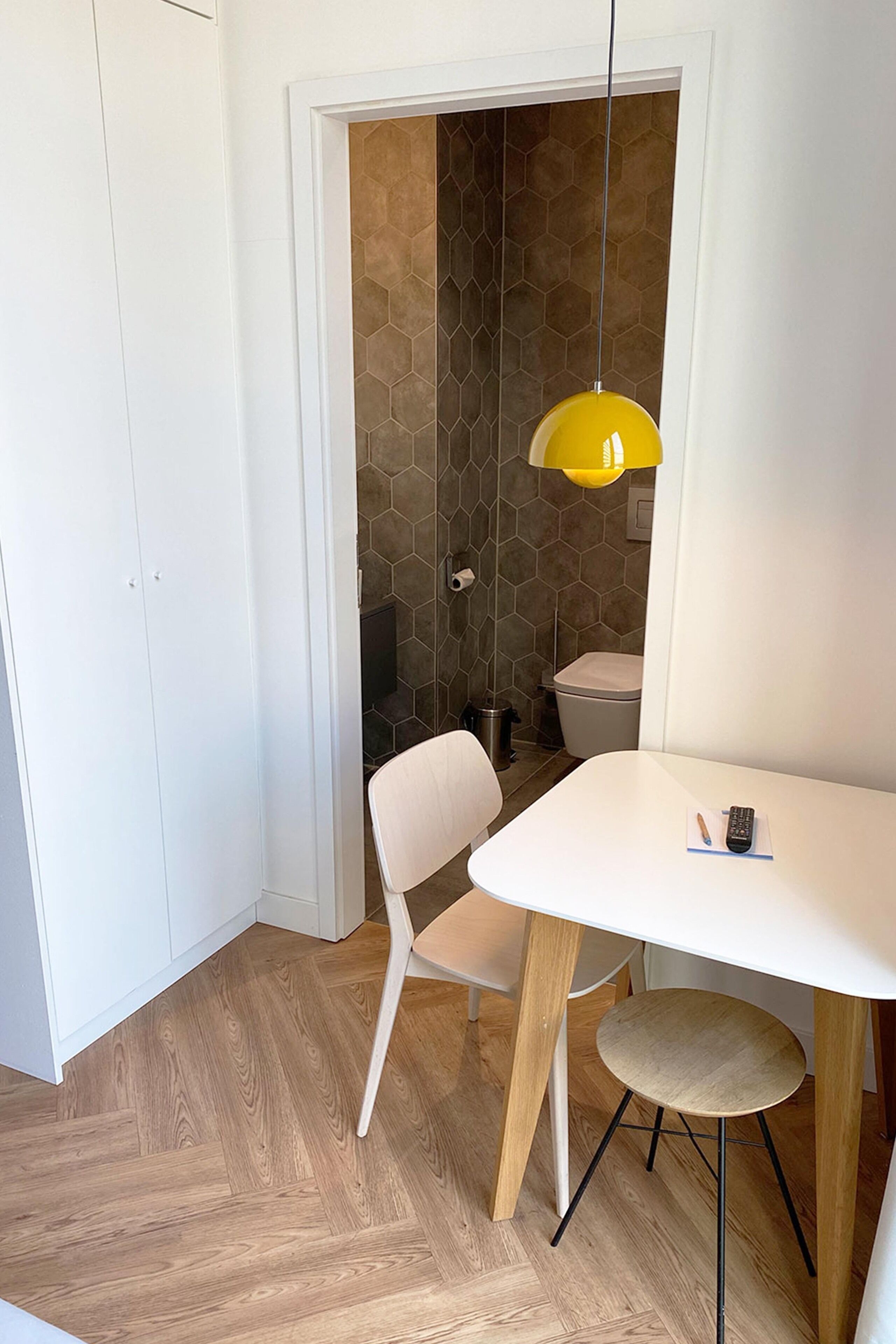 A modern bathroom with a white door, a white sink, and a yellow pendant light.