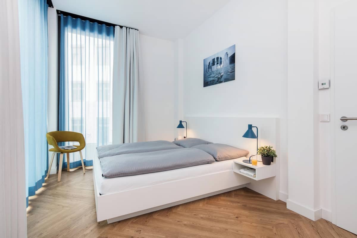 A modern bedroom with a bed, bedside tables, a chair, and a window with curtains.