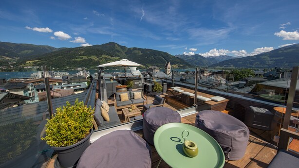 Una terraza en la azotea con mobiliario exterior, vista a un lago y montañas al fondo.