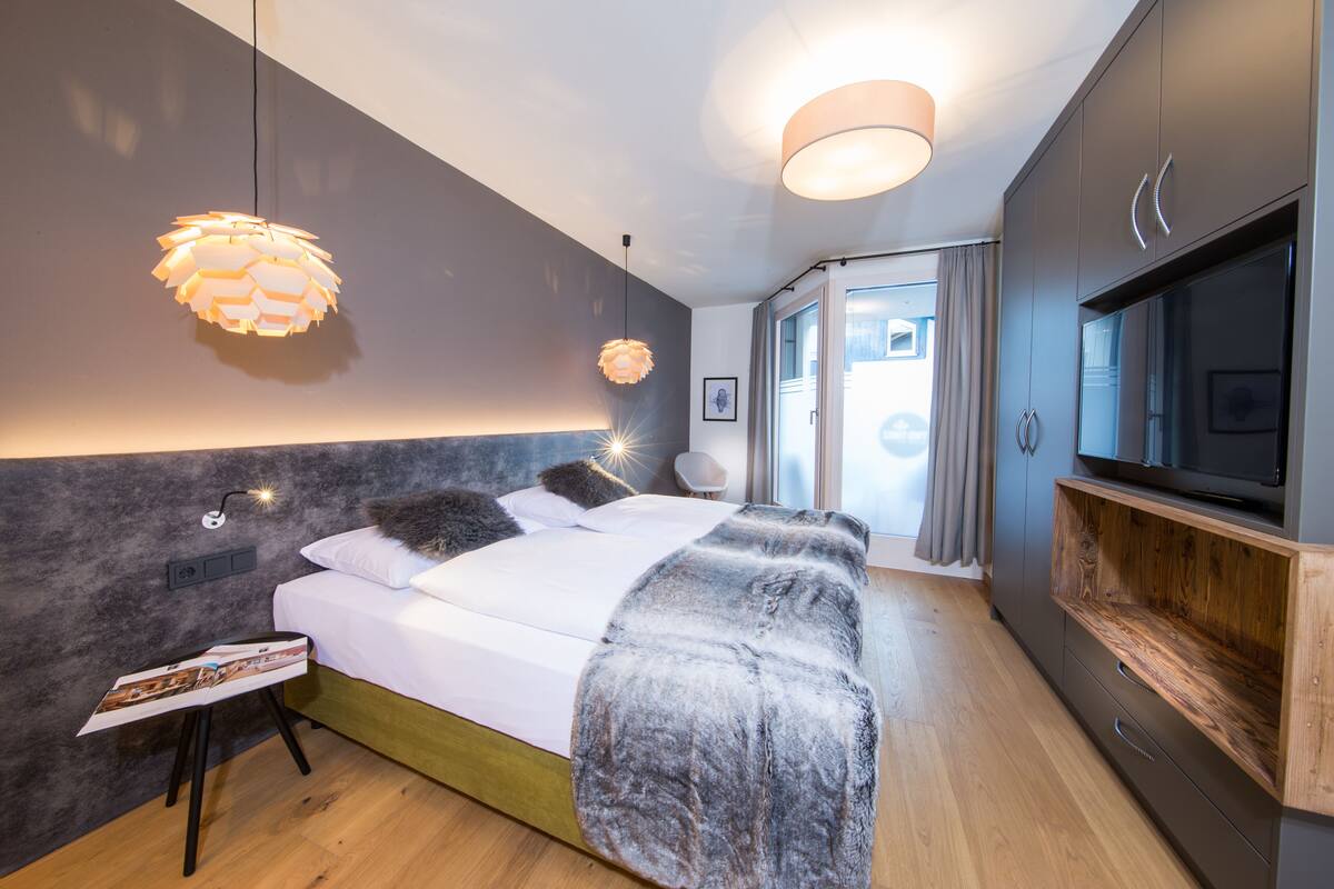 Een moderne slaapkamer met een bed, nachtkastjes, een televisie en een groot raam.