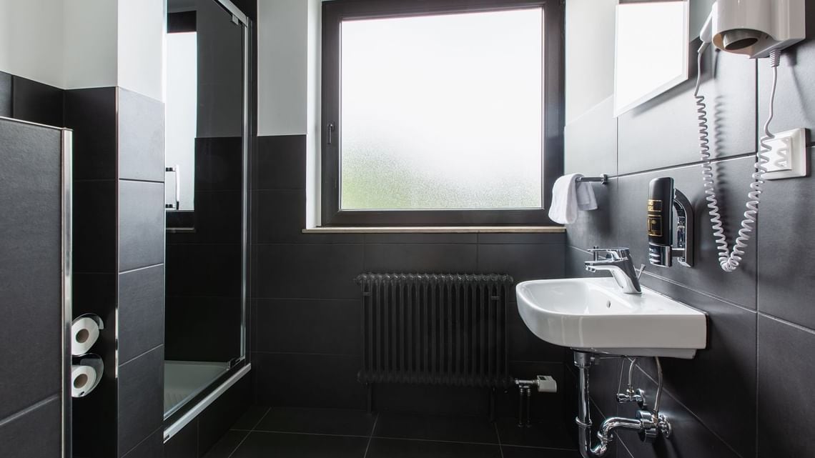 Un baño moderno con un ventanal grande, un lavamanos blanco y un secador de pelo fijado en la pared.