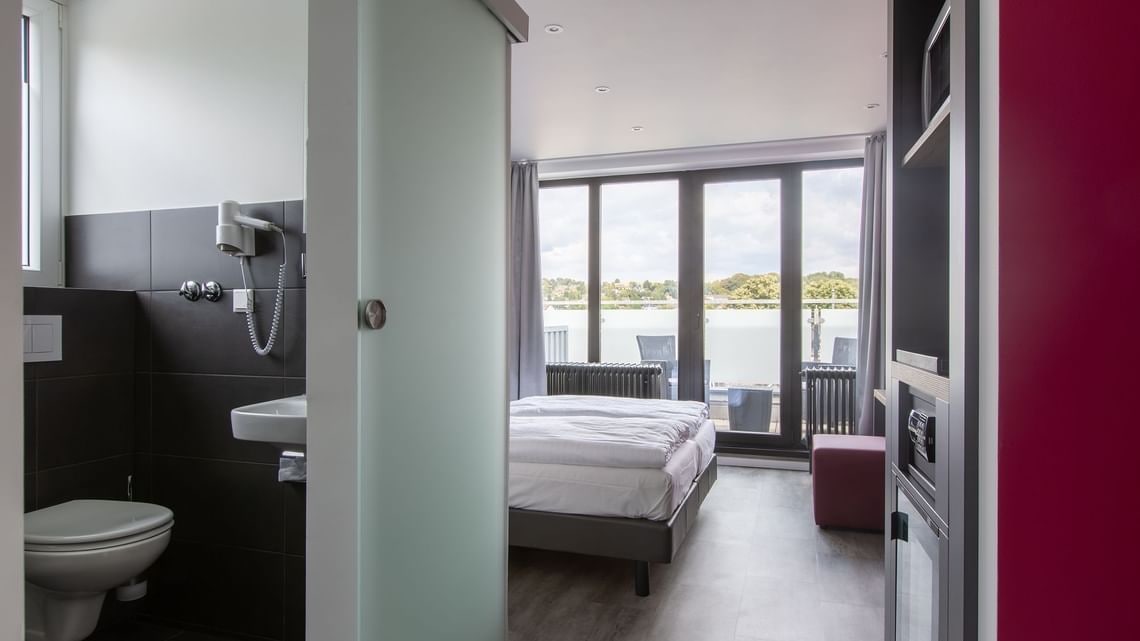 Ein modernes Schlafzimmer mit einem großen Bett, ein Badezimmer mit Toilette und Waschbecken sowie ein Balkon mit Blick aufs Wasser.