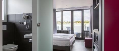 Ein modernes Schlafzimmer mit einem großen Bett, ein Badezimmer mit Toilette und Waschbecken sowie ein Balkon mit Blick aufs Wasser.