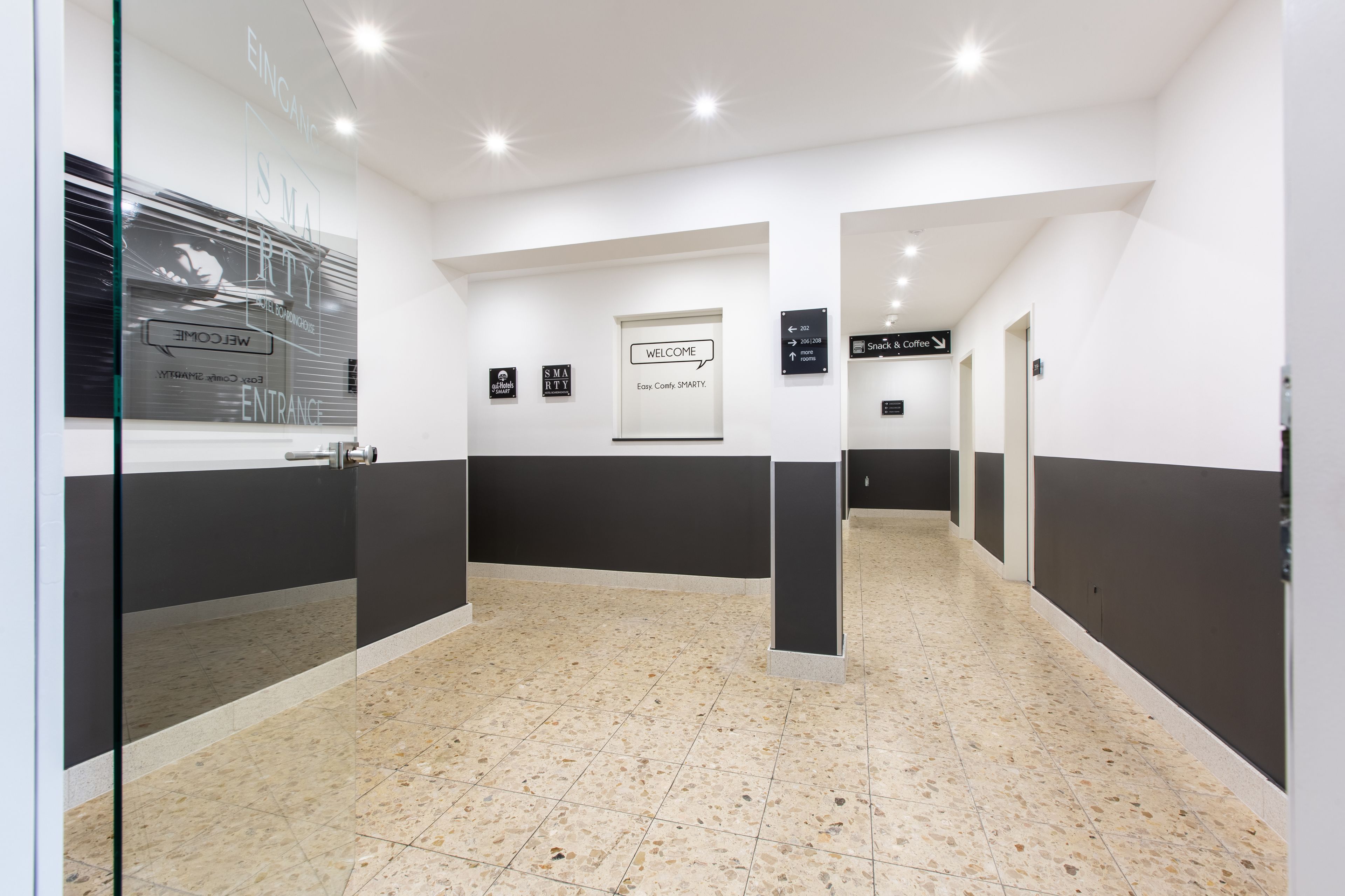 Een moderne hal met richtingaanwijzingen, een welkomstbord en een glazen deur met de tekst 'ENTRANCE'.