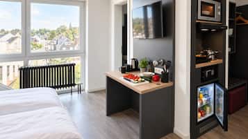 Habitación de hotel moderna con cama, kitchenette pequeña, televisión y vista a la ciudad.