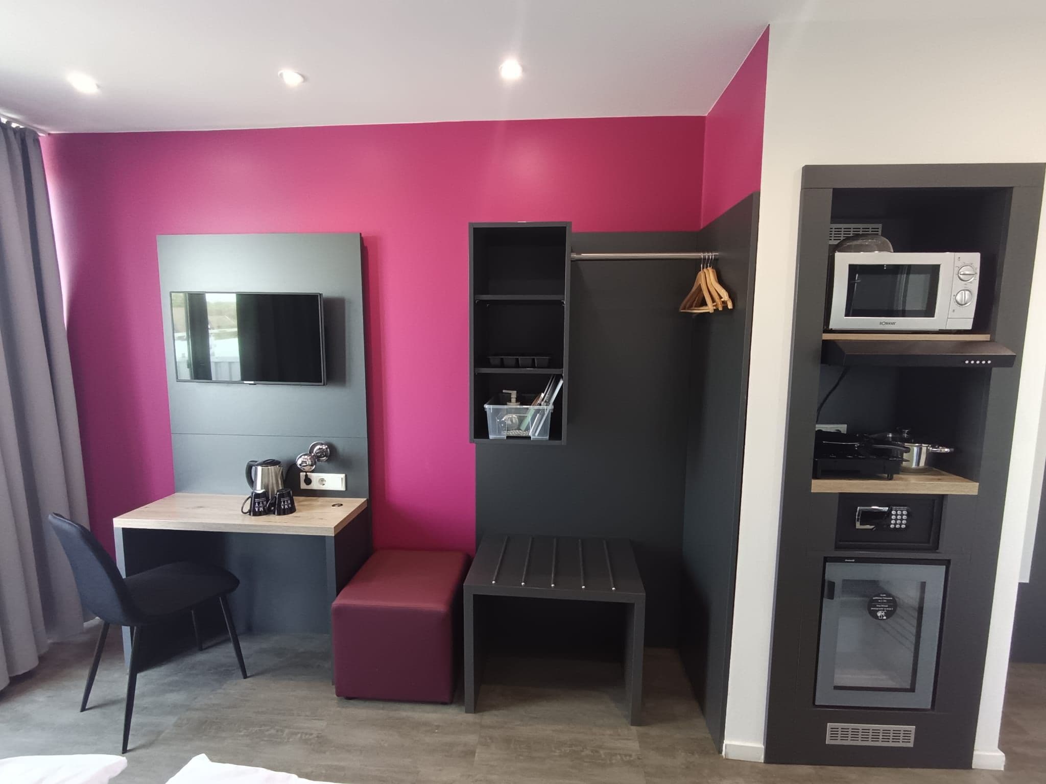 Una habitación compacta con escritorio, una banca, televisión montada en la pared, microondas y un mueble pequeño.