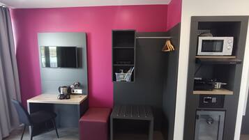 Una habitación compacta con escritorio, una banca, televisión montada en la pared, microondas y un mueble pequeño.