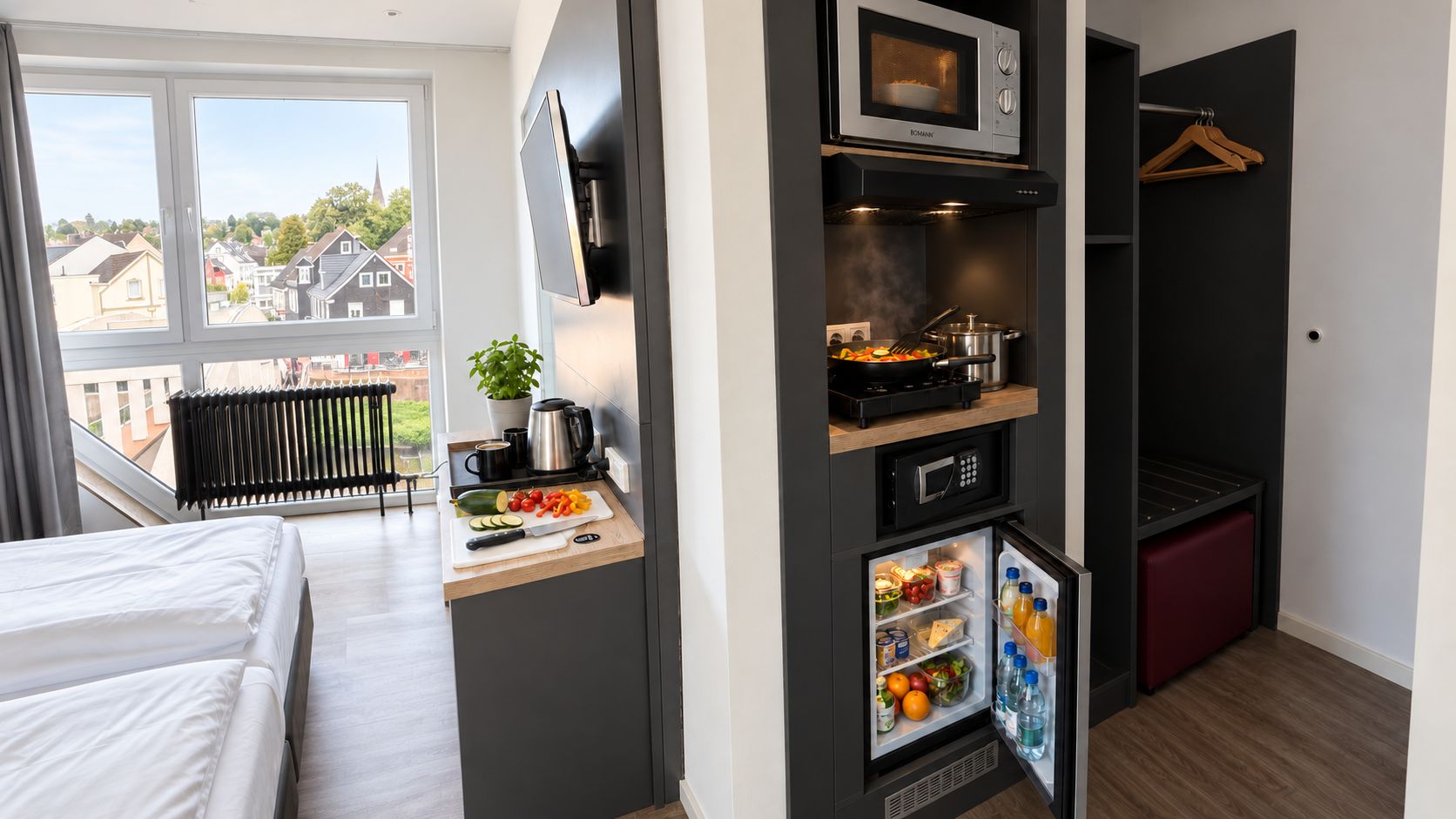 A compact hotel room with a kitchenette, a bed, a small dining area, and a view of the outside.