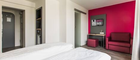 A modern hotel room with a bed, a desk, a red chair, and a bright pink accent wall.
