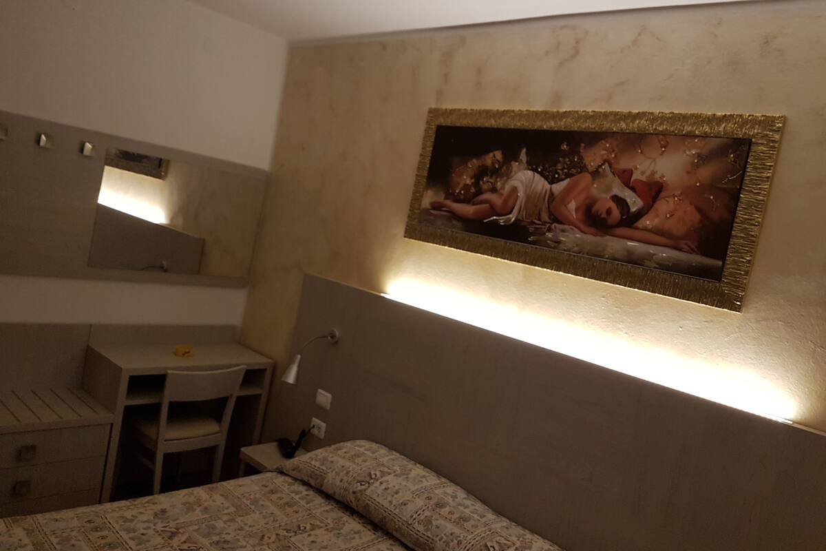 Ein Schlafzimmer mit Bett, Schreibtisch und Stuhl. Ein Gemälde hängt an der Wand.