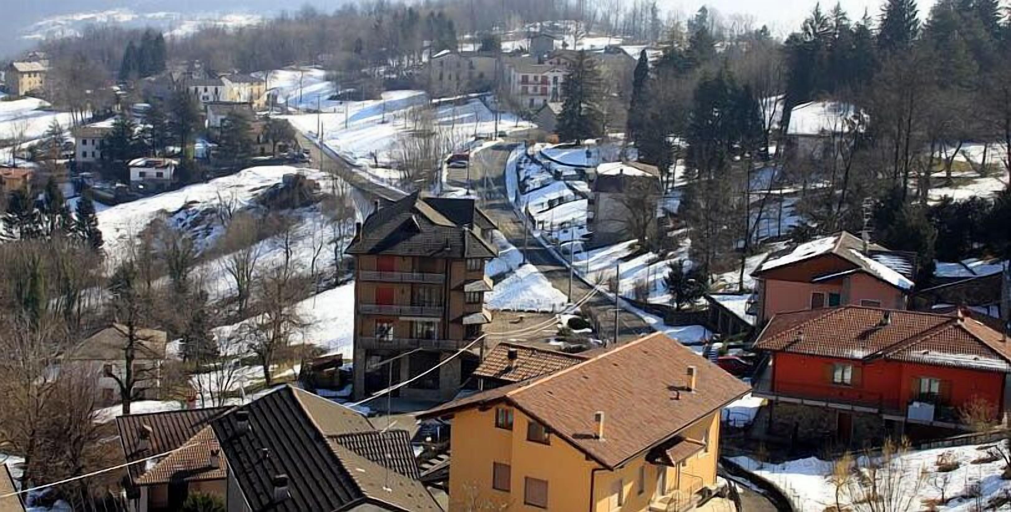A snow-covered village with traditional buildings, including a prominent red house and a yellow building with a sloped roof.