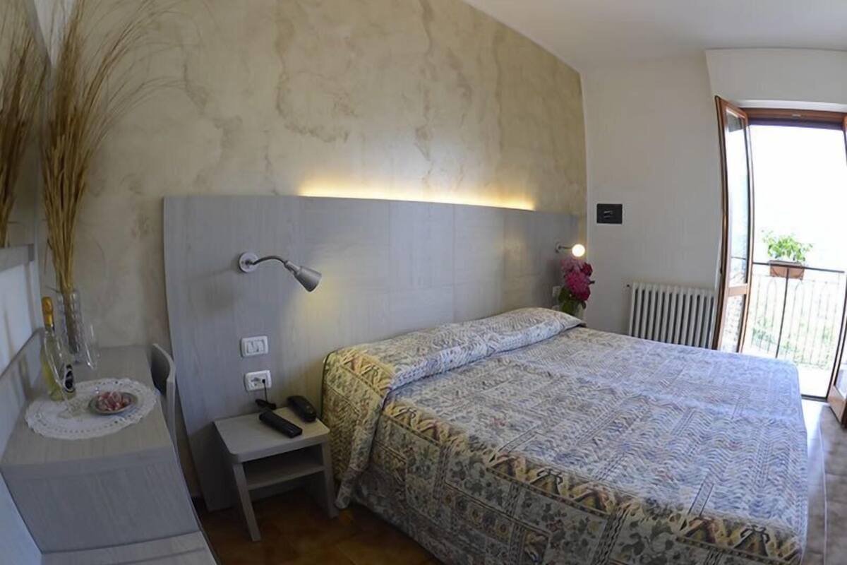 Ein Schlafzimmer mit einem großen Bett, Nachttisch, Lampe und Blick ins Freie.