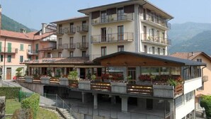 Um hotel com vários andares, varandas, um restaurante no nível térreo e vista para montanhas ao fundo.