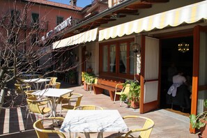 An outdoor cafe area with tables and chairs, a wooden bench, and potted plants.