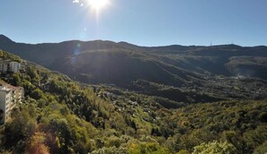 A mountainous landscape with a valley, buildings on the left, and a clear sky.