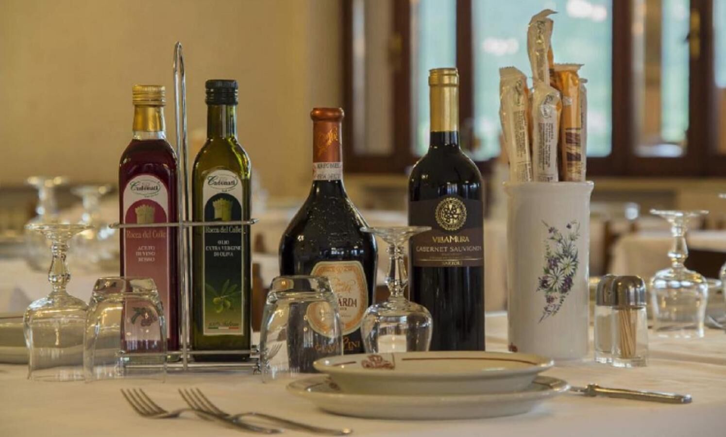 Une table dressée pour le dîner, avec différentes bouteilles de vin, des verres et des couverts.