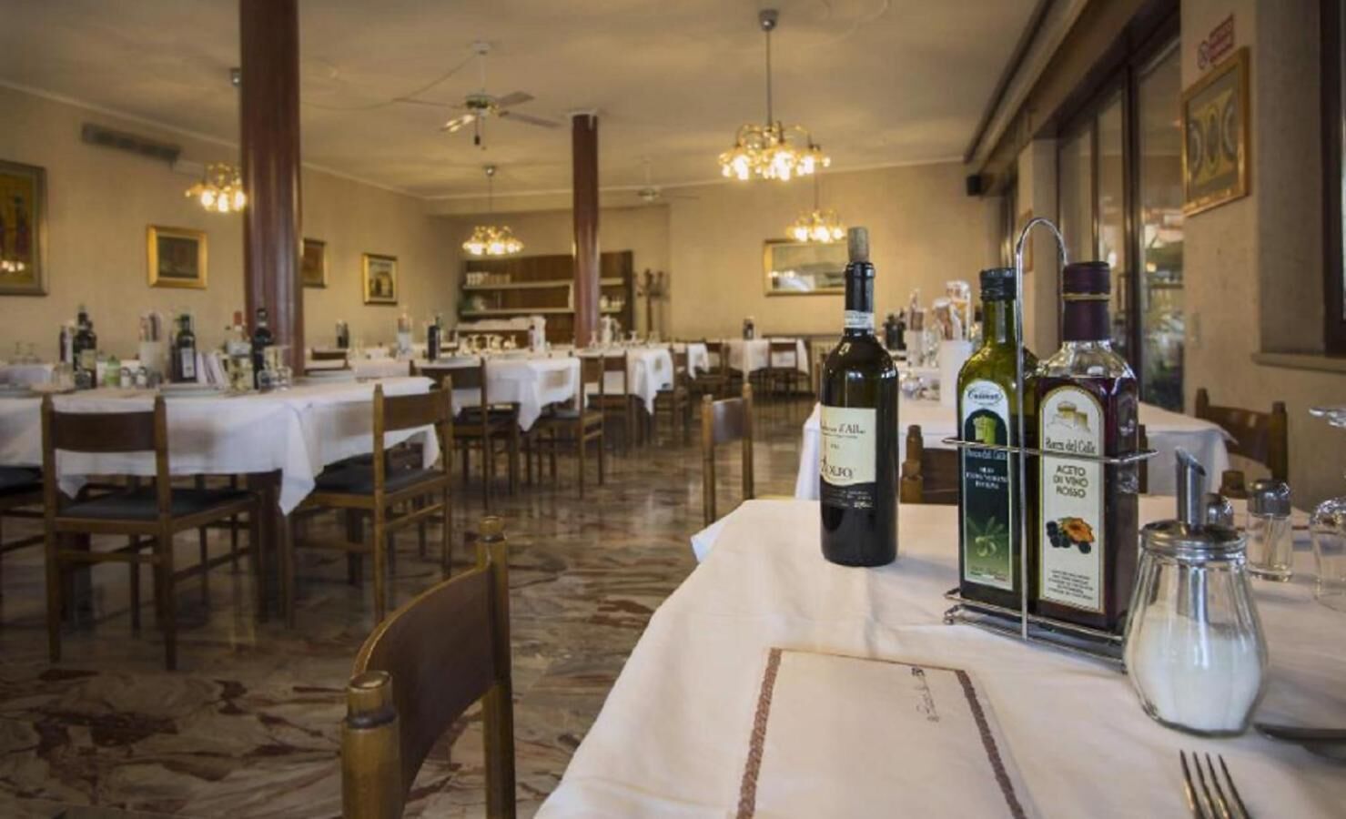 A restaurant with multiple tables, some with white tablecloths, and a variety of bottles and glasses on the tables.