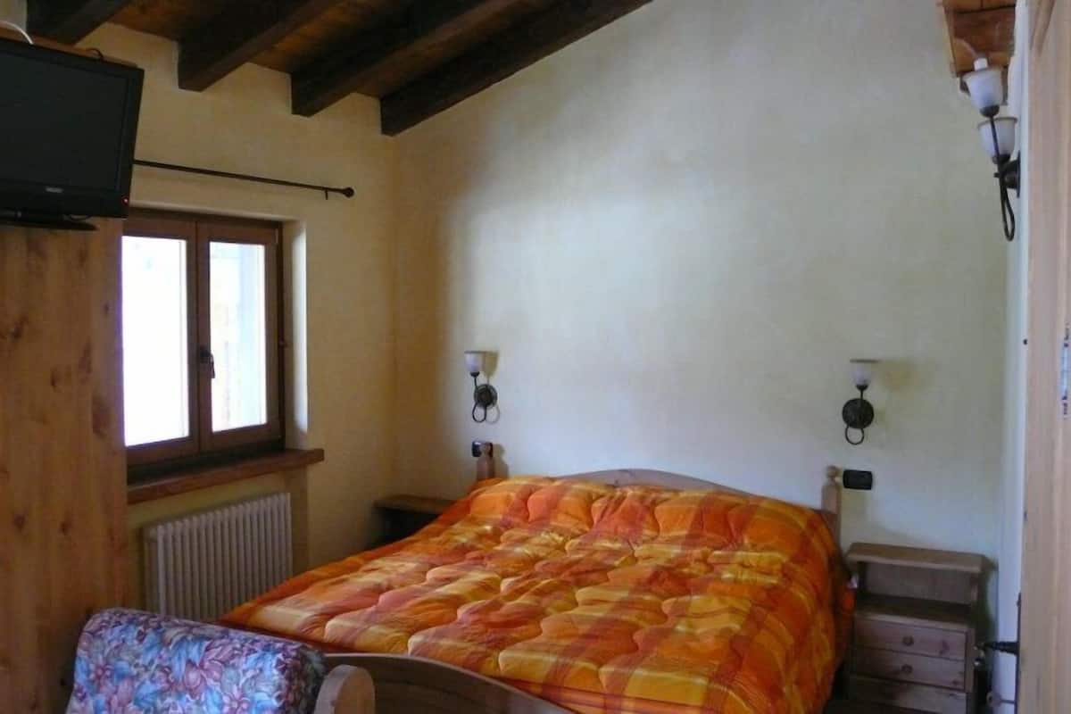 A bedroom with a bed, a chair, a television, and a window.