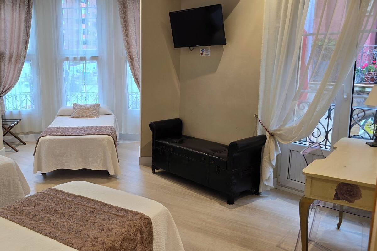 Une chambre d’hôtel avec deux lits, un canapé, une télévision et un balcon agrémenté de plantes.