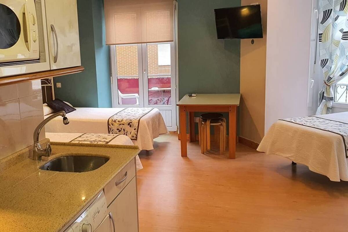 Une pièce compacte comprenant un coin cuisine, un lit, une petite table et un téléviseur.
