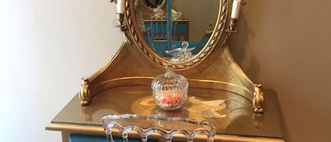 A wooden desk with a gold-framed mirror, a blue chair, and a crystal vase with beads.
