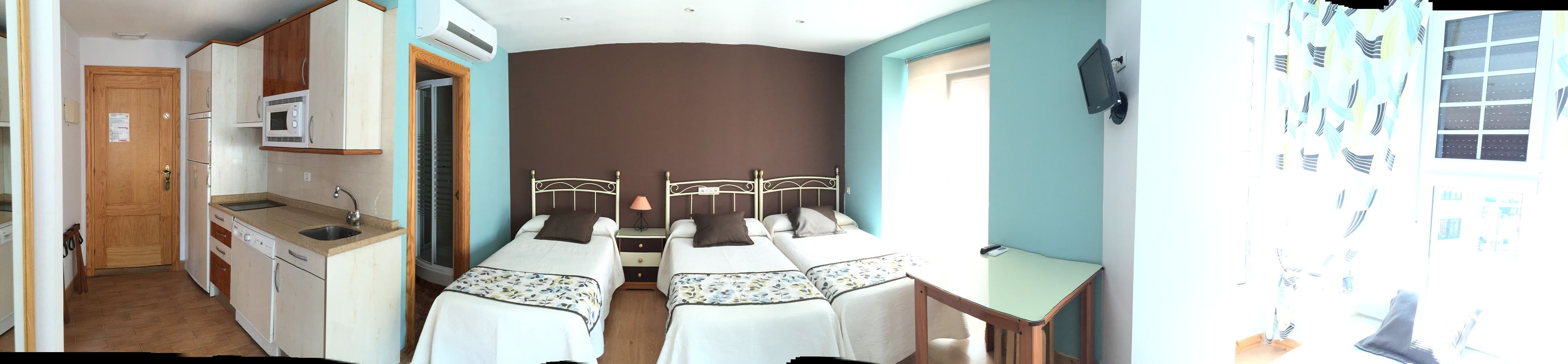 A compact room with a kitchenette, two beds, a small table, and a TV.