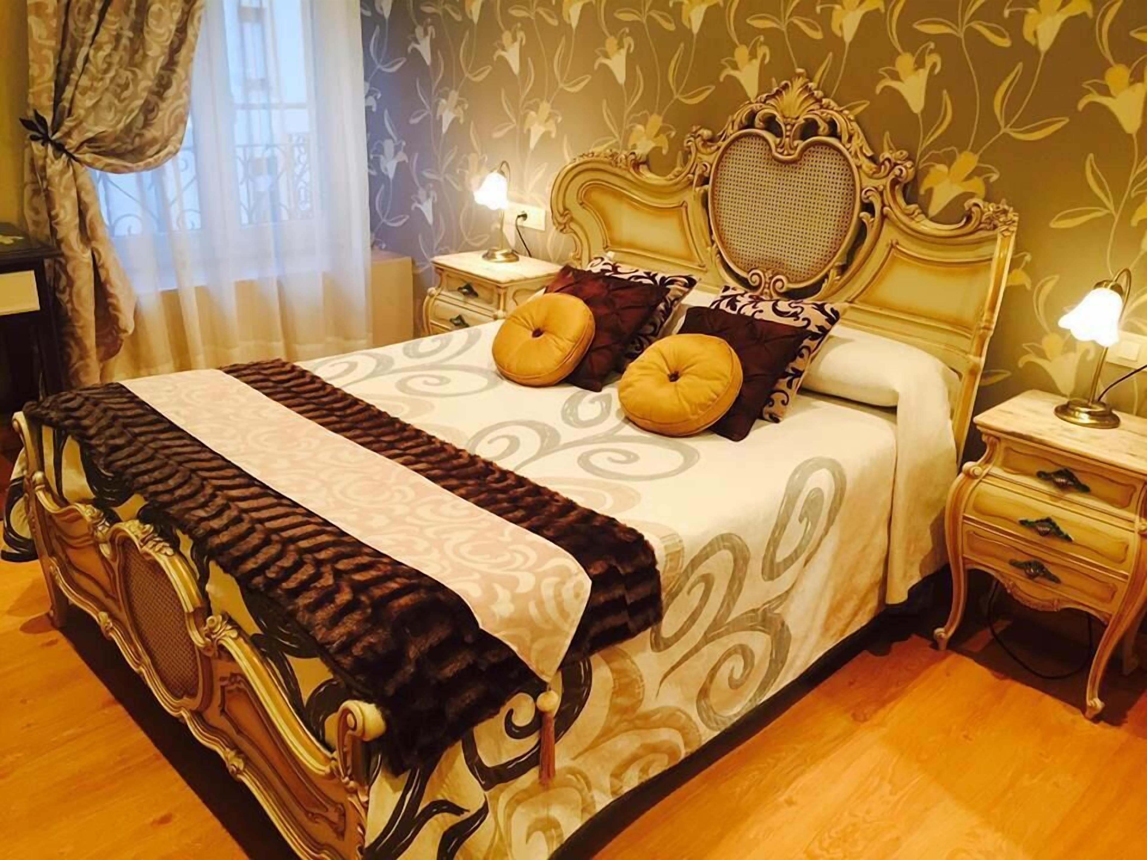 Una cama clásica con dosel, con cabecera y piecera ornamentados, flanqueada por mesitas de noche con lámparas.