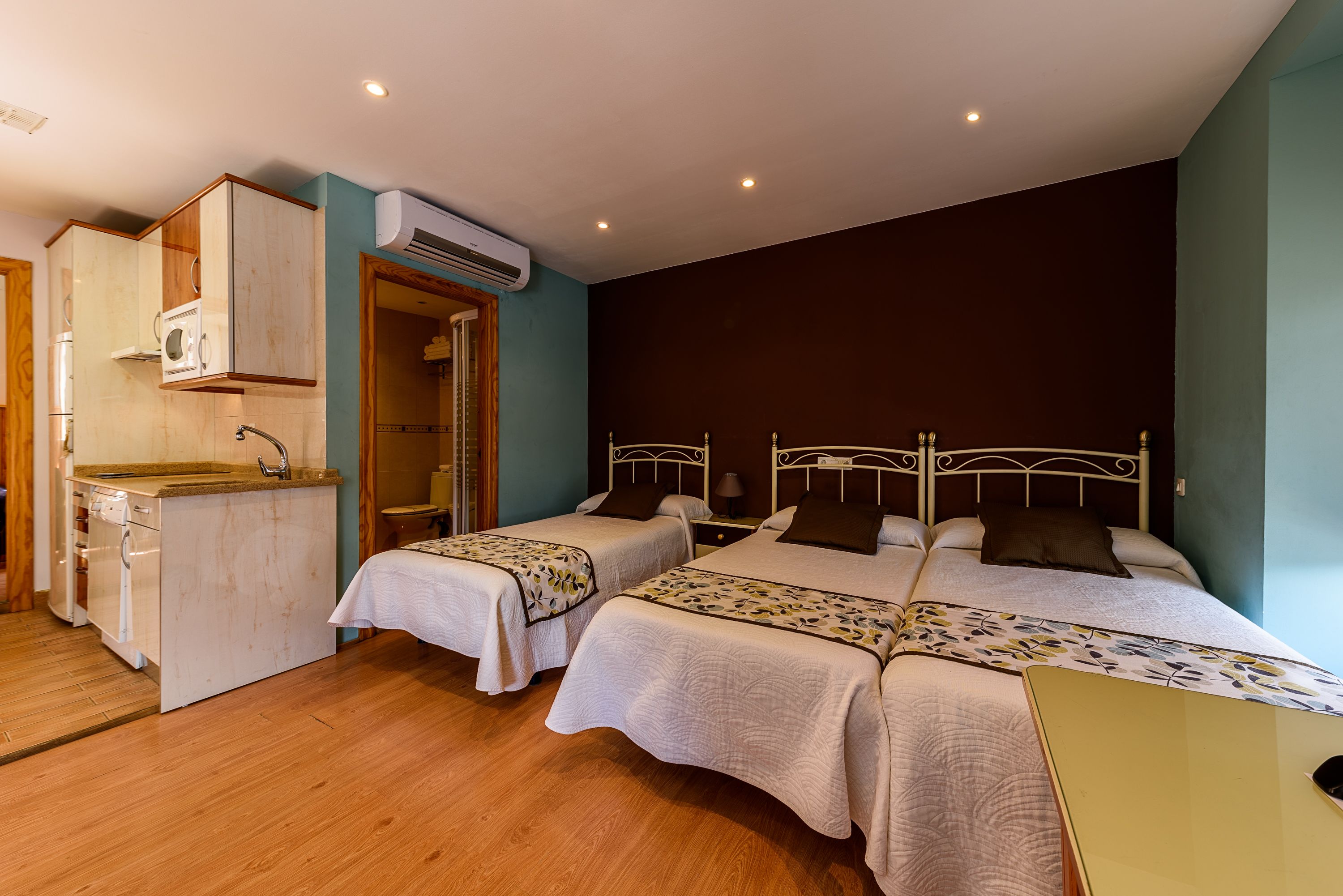 A hotel room with two beds, a kitchenette, and an air conditioning unit.