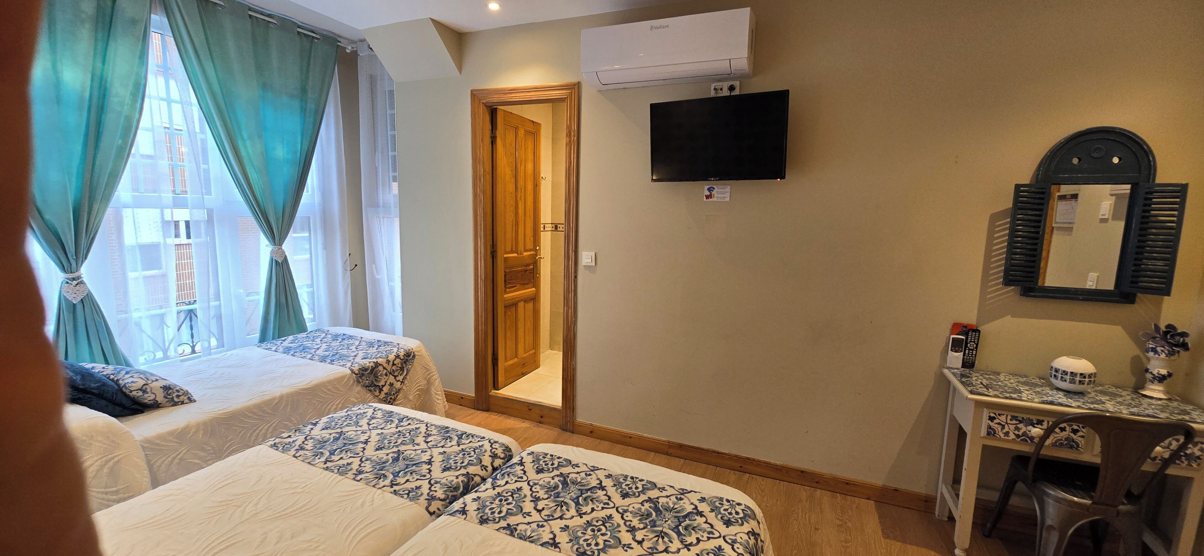 Quarto de hotel com duas camas, televisão, escrivaninha com cadeira e janela com cortinas.