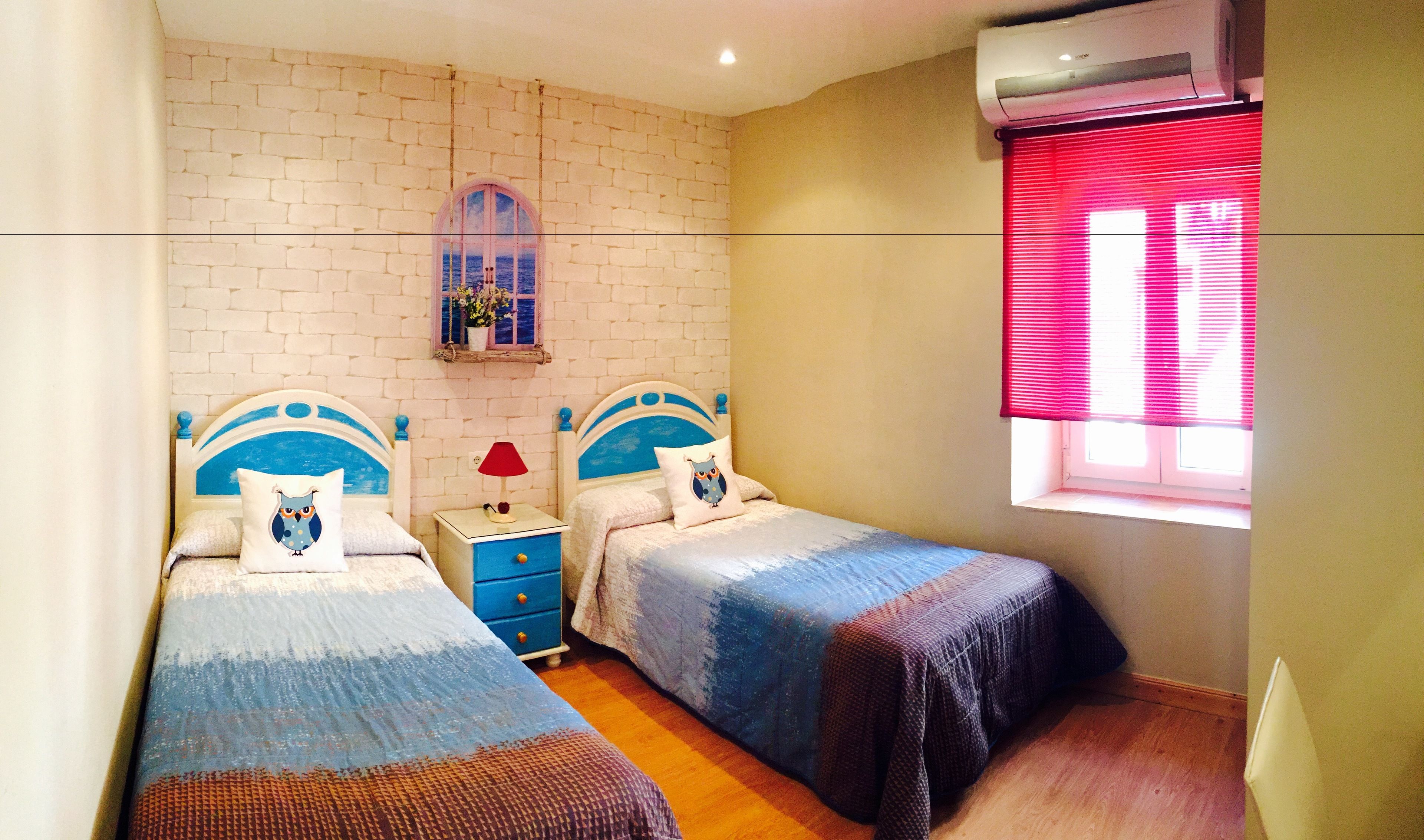 A bedroom with two beds, a nightstand, a window with blinds, and a wall-mounted air conditioner.