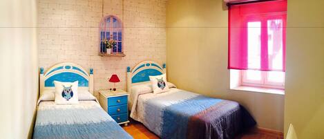 A bedroom with two beds, a nightstand, a window with blinds, and a wall-mounted air conditioner.