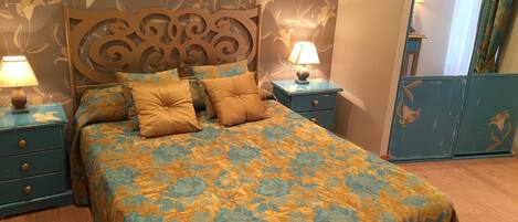 Un dormitorio con una colcha de estampado floral, dos mesitas de noche con lámparas y un cabecero decorativo.