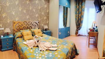 Quarto com colcha floral, cabeceira com espelho decorativo, mesa de cabeceira com abajur e criado-mudo com telefone e carregador.