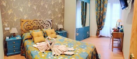 A bedroom with a floral bedspread, a headboard with a decorative mirror, a bedside table with a lamp, and a nightstand with a phone and charger.