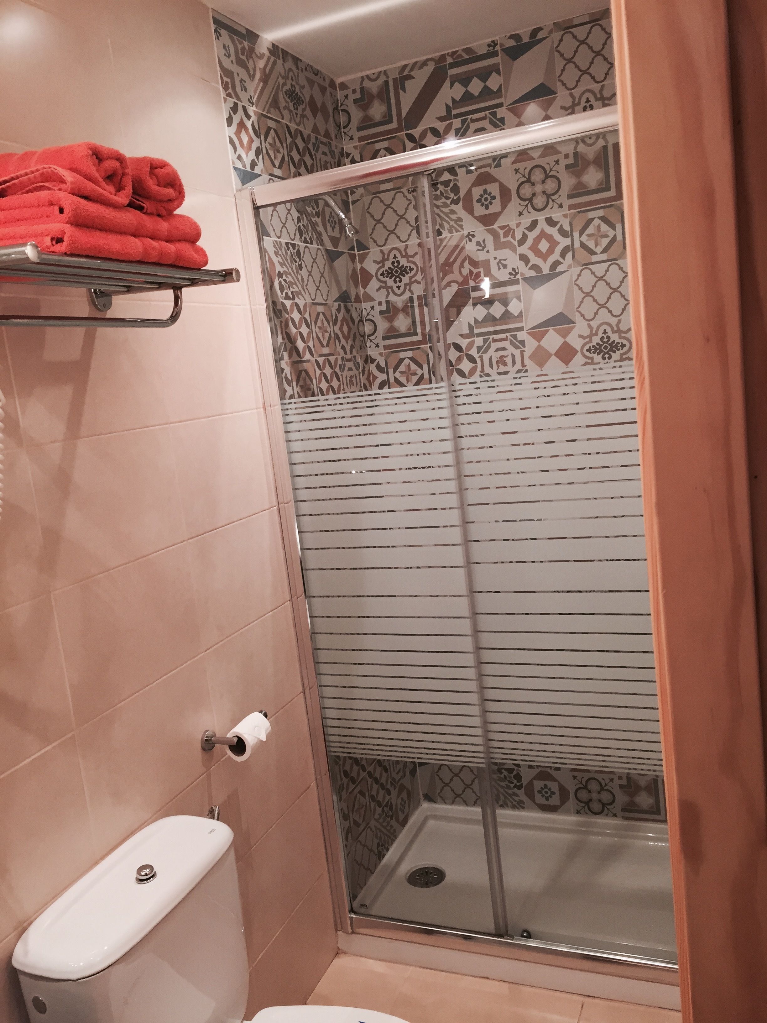 A bathroom with a toilet, a glass shower enclosure, and patterned tiles.