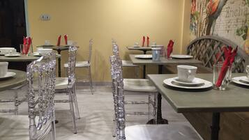 Un espace repas avec des chaises transparentes, des tables dressées avec de l’assiette blanche, des tasses et des serviettes rouges.
