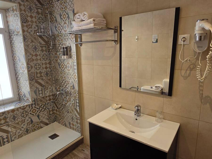 A bathroom with a patterned tile wall, a large mirror, a sink, a towel rack, and a handheld showerhead.