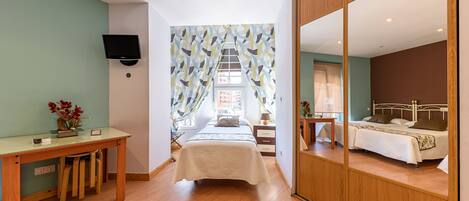 A bedroom with a bed, a desk, a TV, and a mirror.
