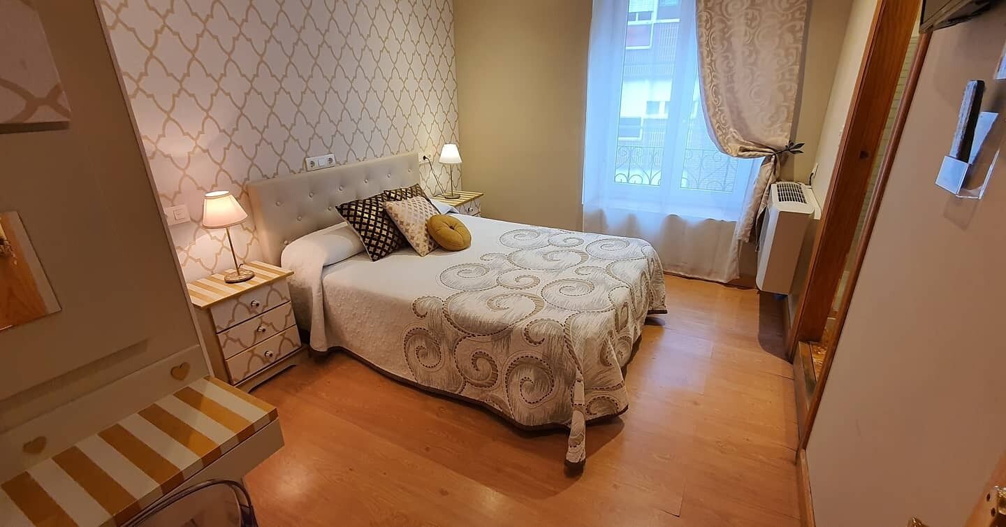 Un dormitorio con cama, mesitas de noche, lámpara, ventana con cortinas y pared con diseño geométrico.