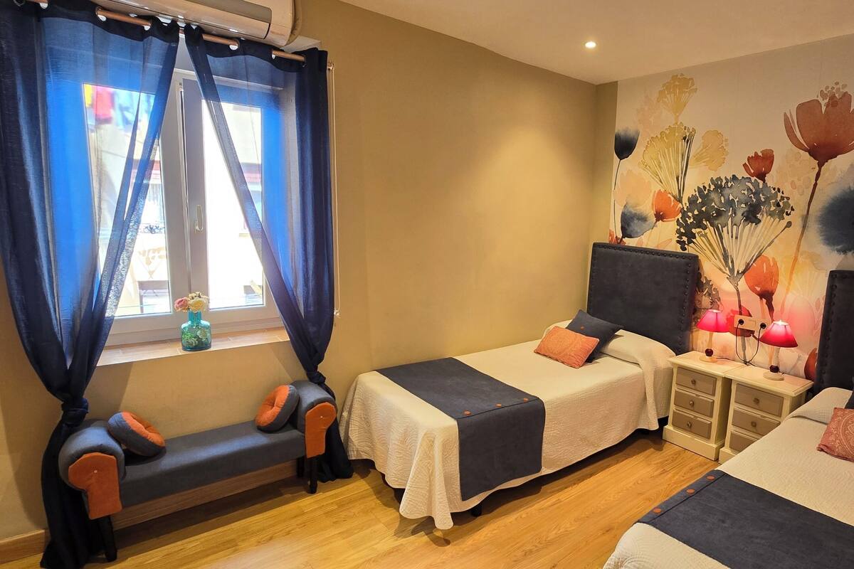 Une chambre d’hôtel avec deux lits simples, un banc, une table de chevet avec des lampes et une décoration murale florale.