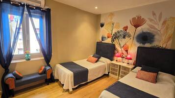 Habitación de hotel con dos camas individuales, un banco, una mesita de noche con lámparas y un mural floral en la pared.