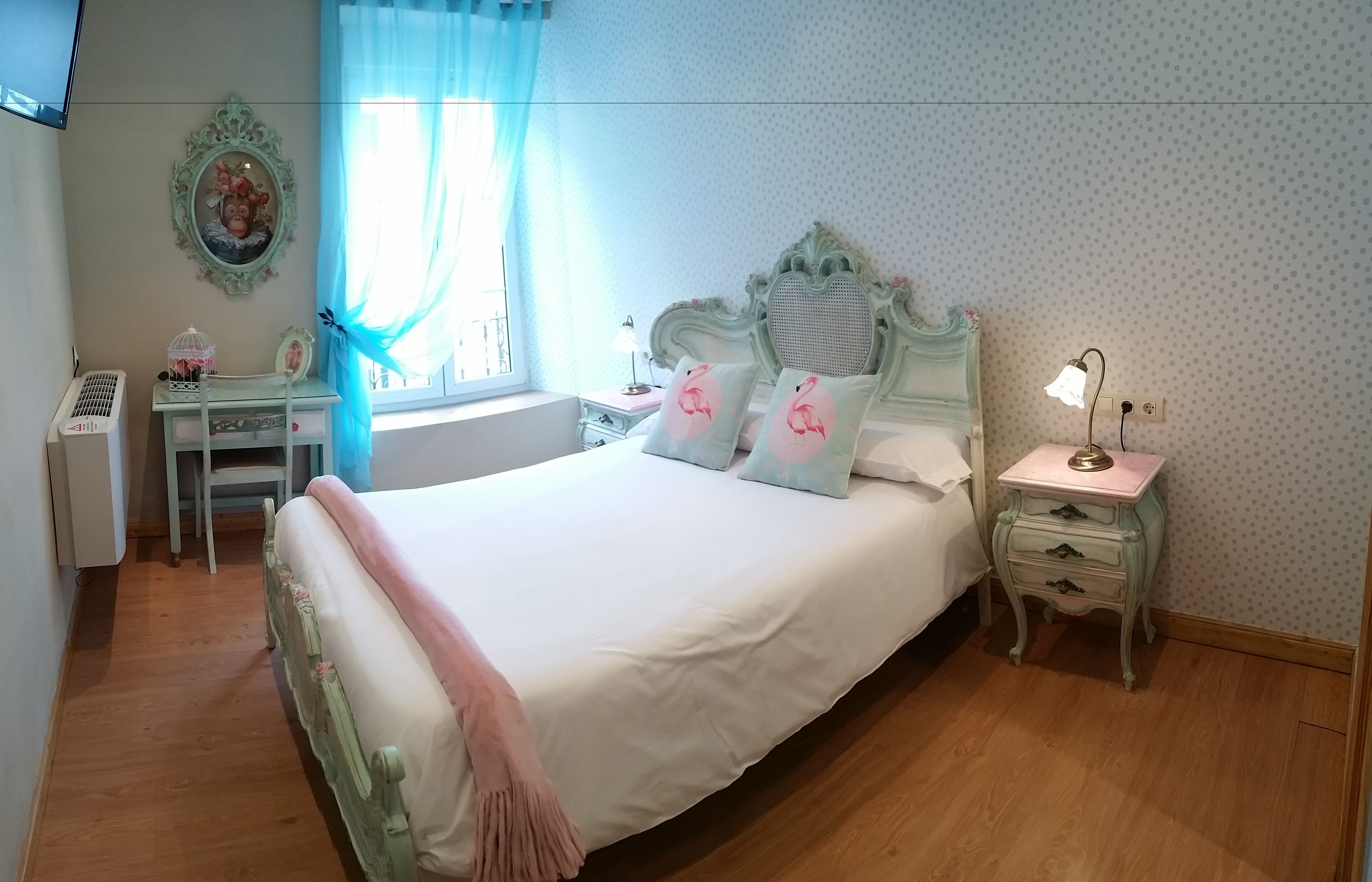 A bedroom with a large bed, a bedside table, a nightstand, a dresser, a window with curtains, and a wall-mounted picture.