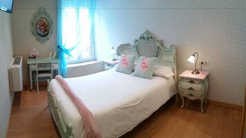 A bedroom with a large bed, a bedside table, a nightstand, a dresser, a window with curtains, and a wall-mounted picture.