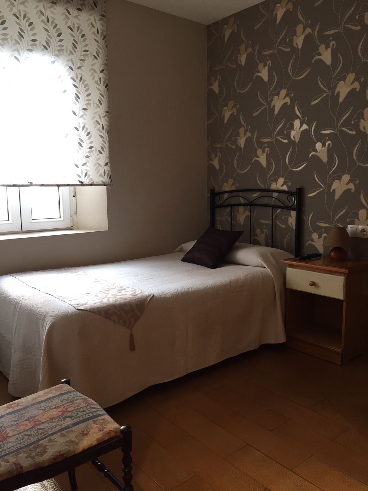 A bedroom with a bed, a nightstand, a chair, and a window with curtains.