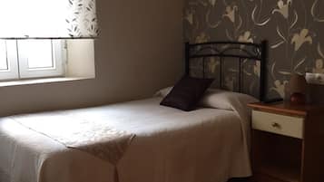 A bedroom with a bed, a nightstand, a chair, and a window with curtains.